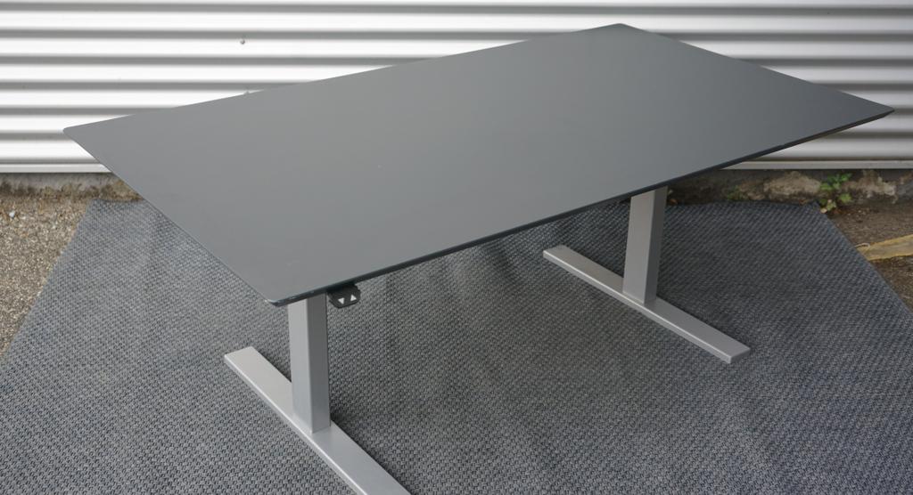 Skråt billede af Holmris hæve-sænkebord 160x90 i antracitgrå med kabelbakke og affasede kanter.